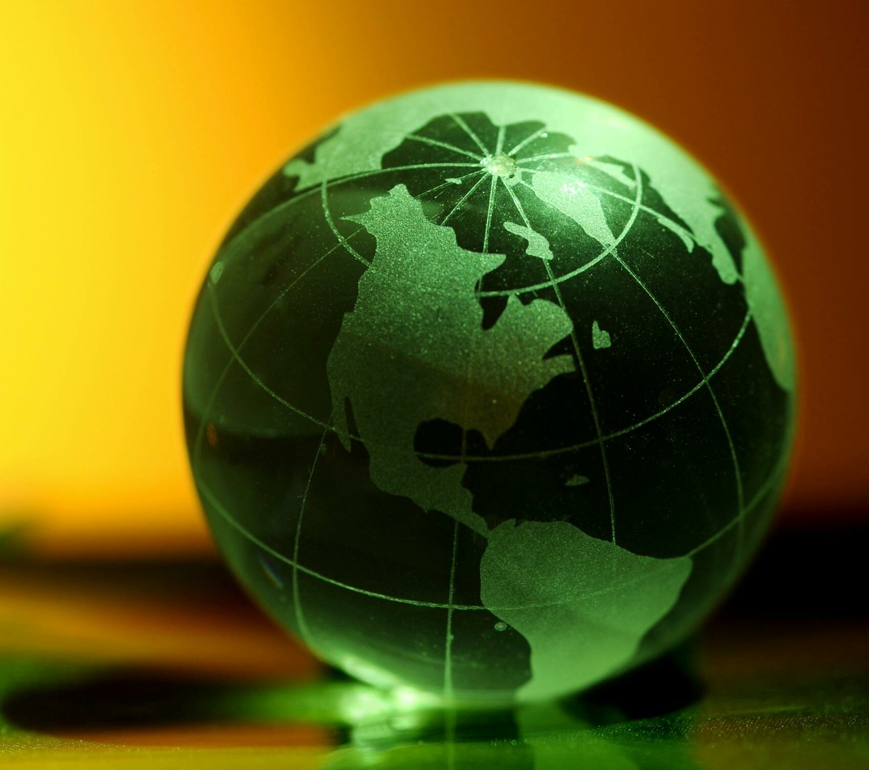 Glass globe with map of continents glows against an orange and green background.